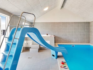 An indoor swimming pool with a blue slide, a ladder, and a small table with a vase and a book. - 5 Star Holiday Home in Grenaa (Grenaa)