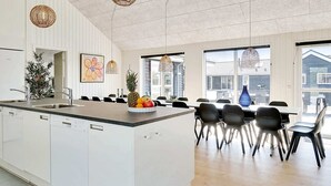 A modern kitchen with a central island, dining area with chairs, and large windows. - 5 Star Holiday Home in Grenaa (Grenaa)