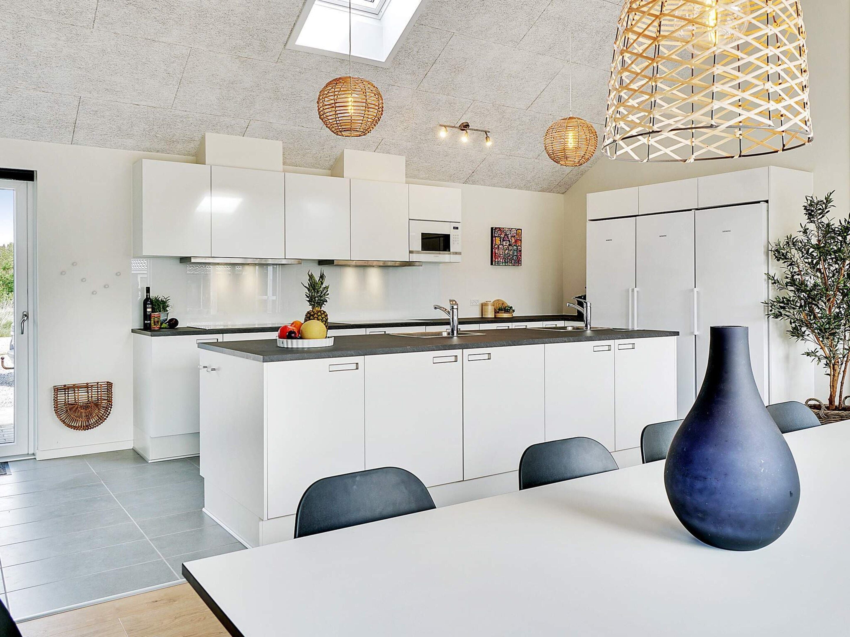 Une cuisine moderne avec des meubles blancs, un îlot central et un coin repas comprenant une table et des chaises.