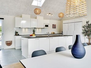 A modern kitchen with white cabinets, a central island, and a dining area with a table and chairs. - 5 Star Holiday Home in Grenaa (Grenaa)
