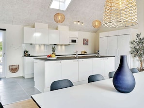 A modern kitchen with white cabinets, a central island, and a dining area with a table and chairs. - 5 Star Holiday Home in Grenaa (Grenaa)