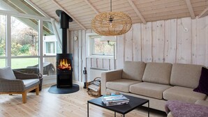 Ein gemütliches Wohnzimmer mit Kaminofen, Korbmöbeln und Blick ins Freie.