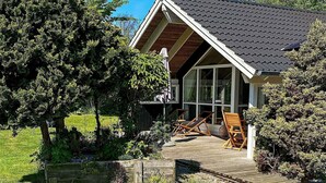 Ein modernes Haus mit Satteldach, großen Fenstern und einer Holzterrasse mit Gartenmöbeln.