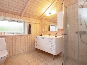 A wooden cabin bathroom with a toilet, a sink with a mirror, and a shower. - Picturesque Holiday Home in Hovedstaden With Sauna (Vejby)