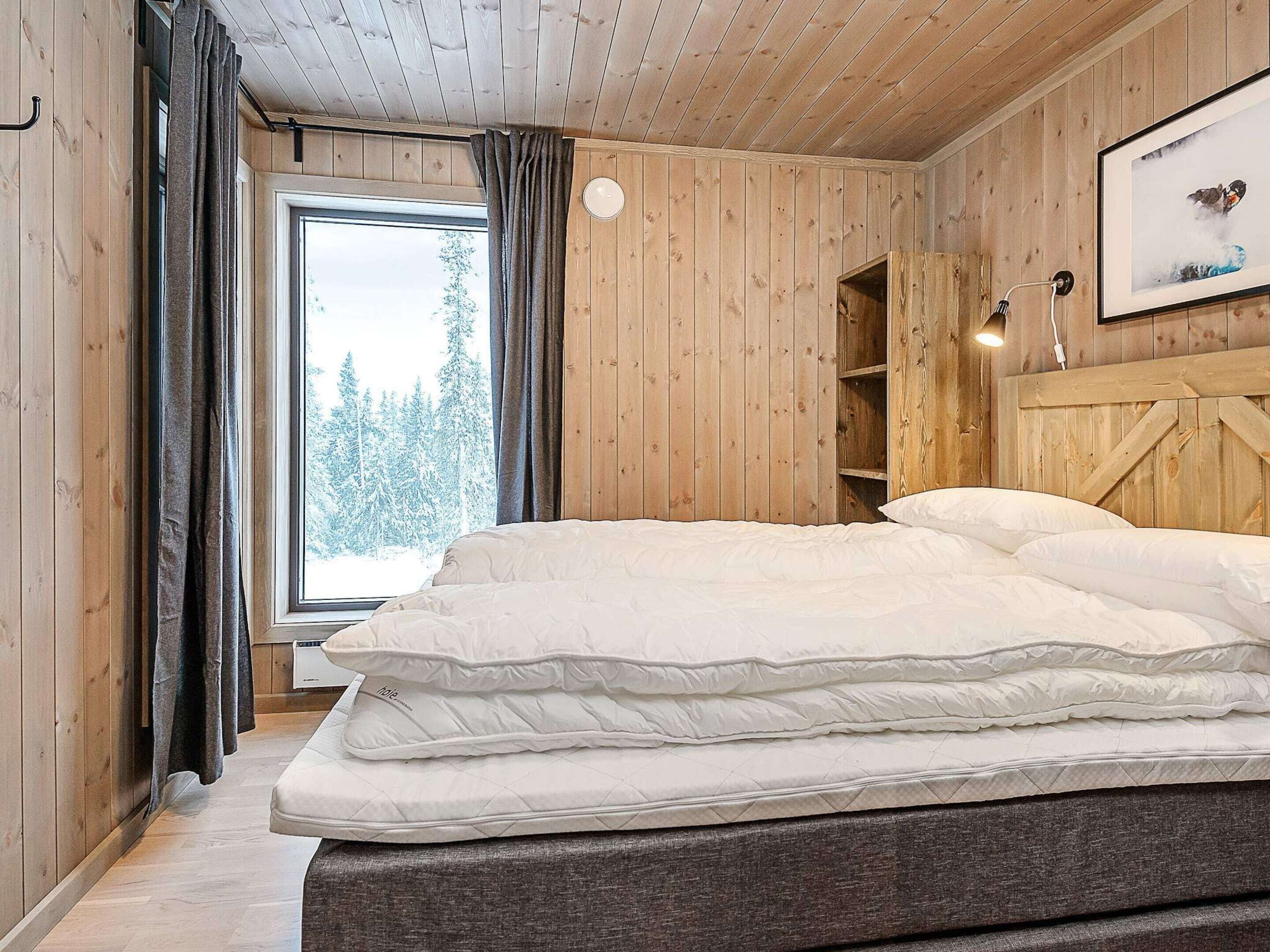 Une pièce en bois avec un lit, une fenêtre avec des rideaux et une étagère sur laquelle est posée une image.