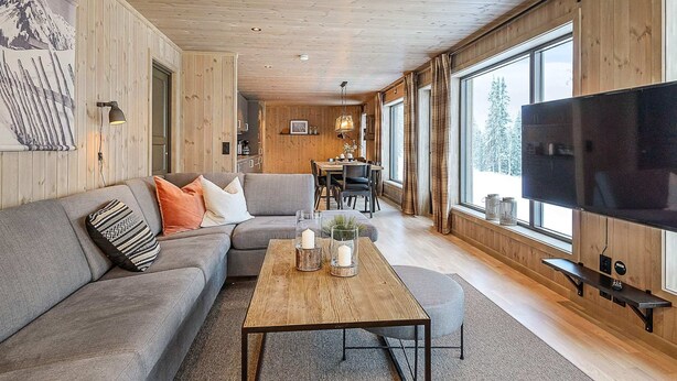 A modern living room with a wooden ceiling, a large flat-screen TV, a sofa, a coffee table, and a dining area with a table and chairs. - 4 Star Holiday Home in Favang (Ringebu)