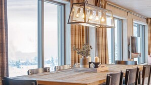 A dining area with a long wooden table, black chairs, a chandelier, and a view of a snowy landscape through large windows. - 4 Star Holiday Home in Favang (Ringebu)