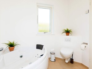 A modern bathroom with a bathtub, toilet, and two potted plants.