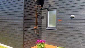 A modern building with a dark exterior, a window with a frosted glass panel, and a small outdoor area with a wooden bench and a potted plant. - 5 Star Holiday Home in Lokken (Lokken)