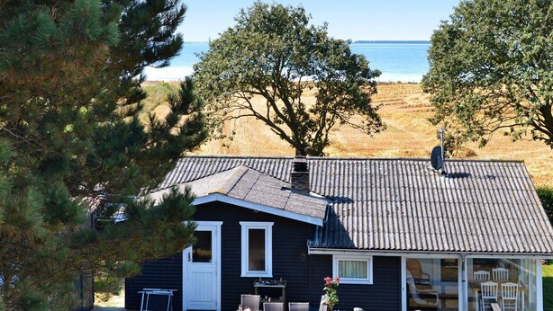 A cabin with a deck, a table, chairs, and a view of the beach and ocean. - 6 Person Holiday Home in Martofte (Martofte)