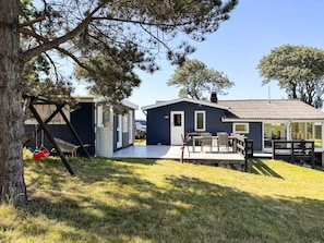 A small cabin with a deck, a swing set, and a car parked nearby.