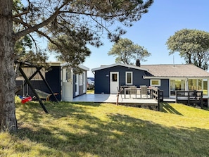 A small, two-story cabin with a deck, a swing set, and a car parked nearby. - 6 Person Holiday Home in Martofte (Martofte)