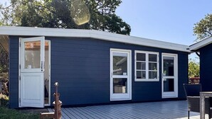 A dark blue house with white-framed windows, a wooden deck, and a small outdoor seating area. - 6 Person Holiday Home in Martofte (Martofte)