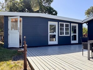 A dark blue house with white-framed windows, a wooden deck, and a small outdoor seating area.
