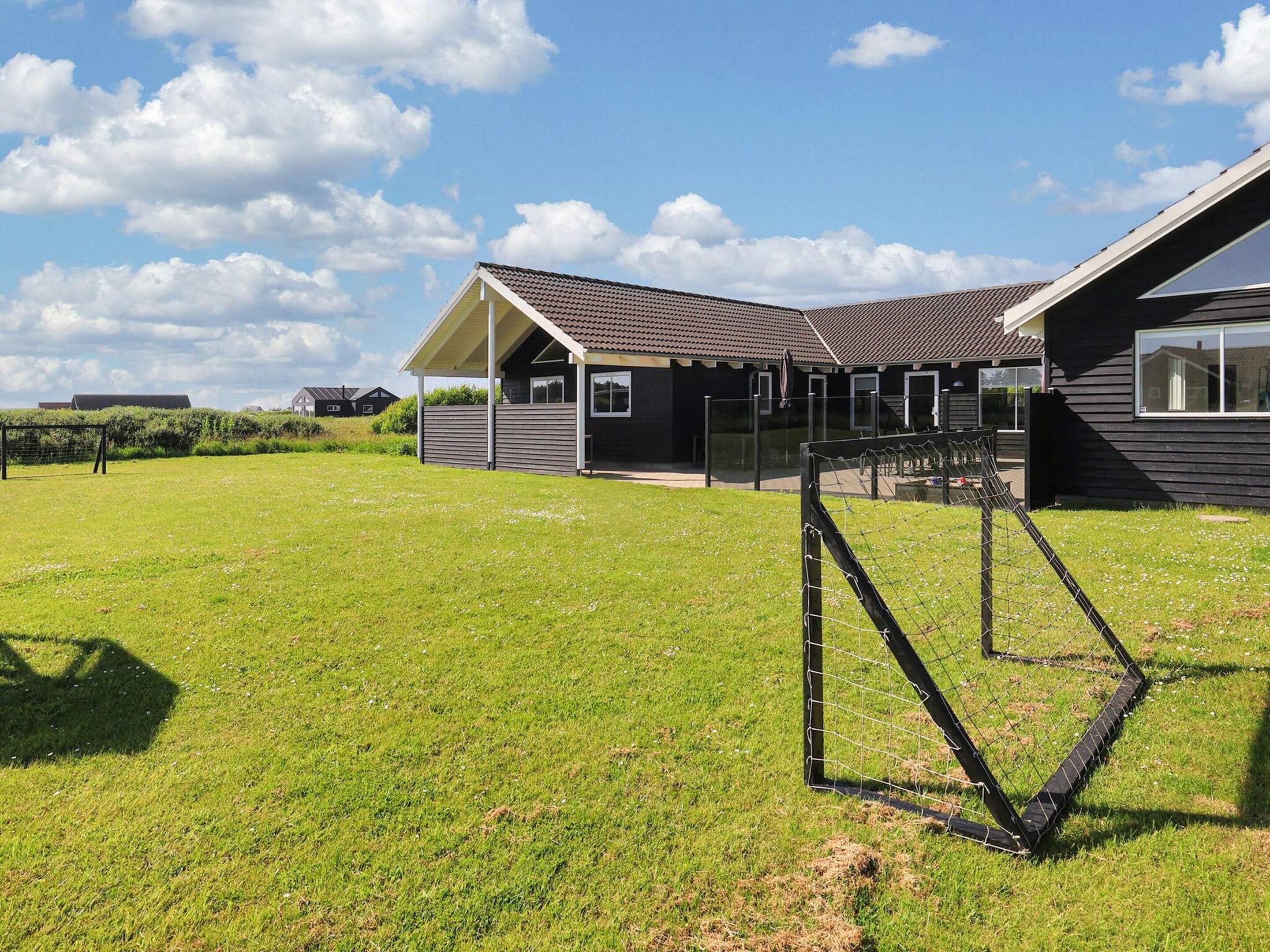 Een woonhuis met een groot gazon, een overdekt terras en een huis met schuin dak.