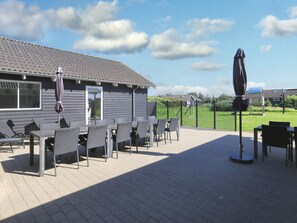An outdoor patio area with tables and chairs, a covered seating area, and a view of a residential neighborhood.