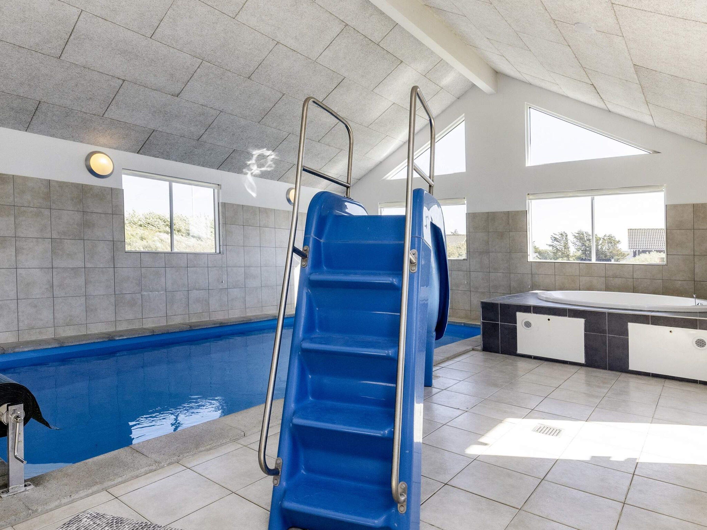 En swimmingpool med en blå rutsjebane, et spabad og udsigt over naturen gennem store vinduer.