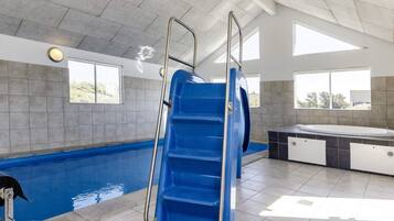 En swimmingpool med en blå rutsjebane, et spabad og udsigt over naturen gennem store vinduer.