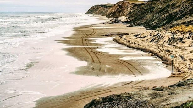 Une plage côtière avec un rivage sablonneux, des falaises et une vue dégagée sur l’océan.