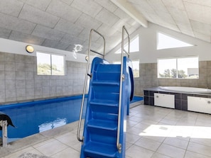 A swimming pool with a blue slide, a hot tub, and a tiled floor.