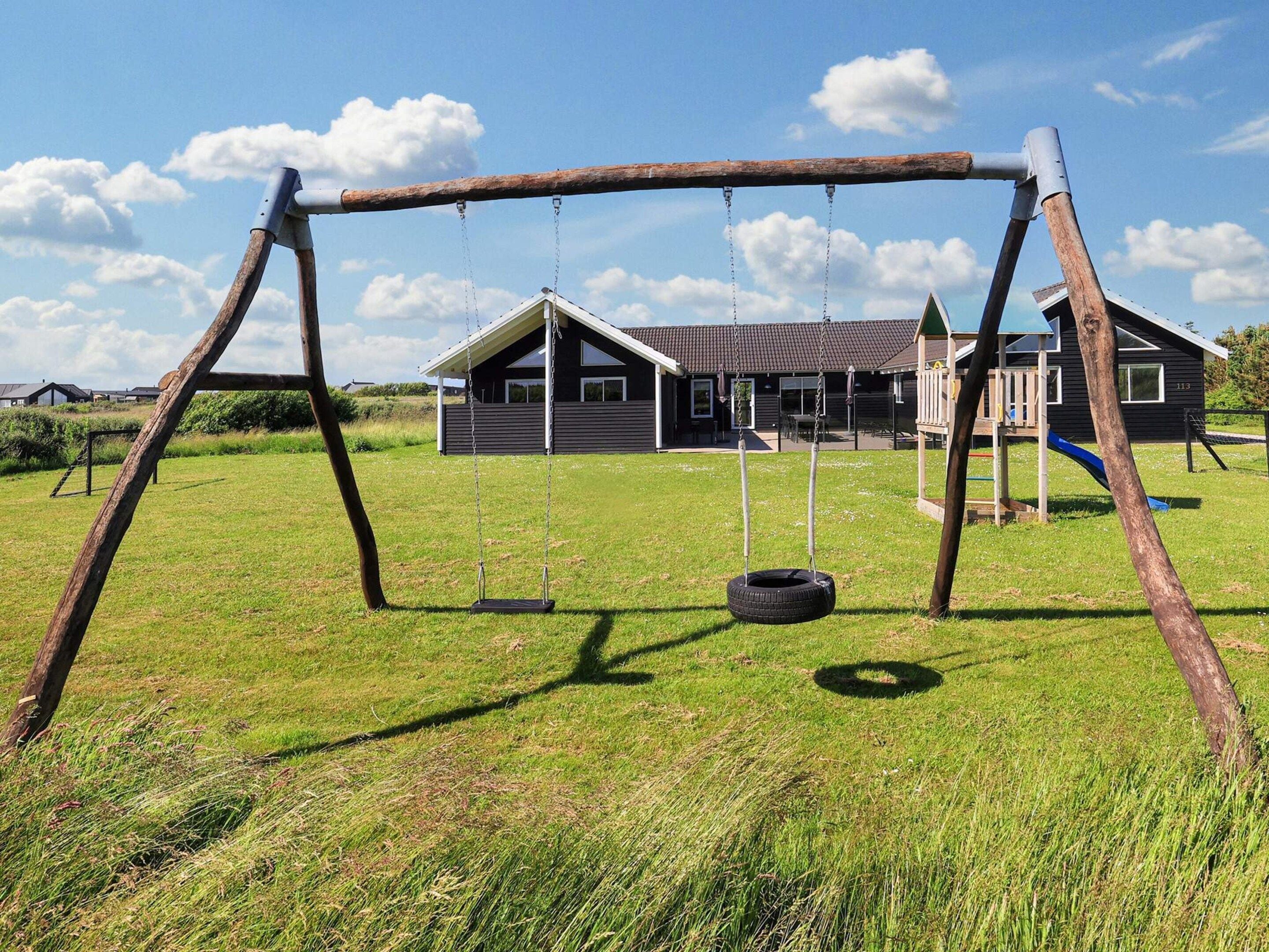 A swing set with a tire swing in a grassy field, a wooden structure, and a building in the background.
