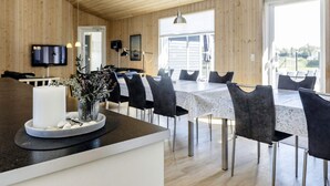 Un espace de repas moderne avec un plafond en bois, un îlot central agrémenté d’une bougie blanche et de plantes décoratives, et une grande fenêtre qui laisse entrer la lumière naturelle.