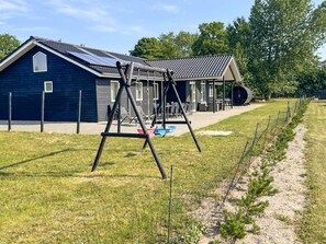 A building with a covered patio area, a swing set, and a fenced garden.