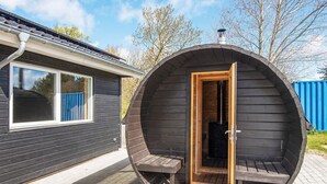 A wooden sauna with a door open, a bench inside, and a chimney on top.