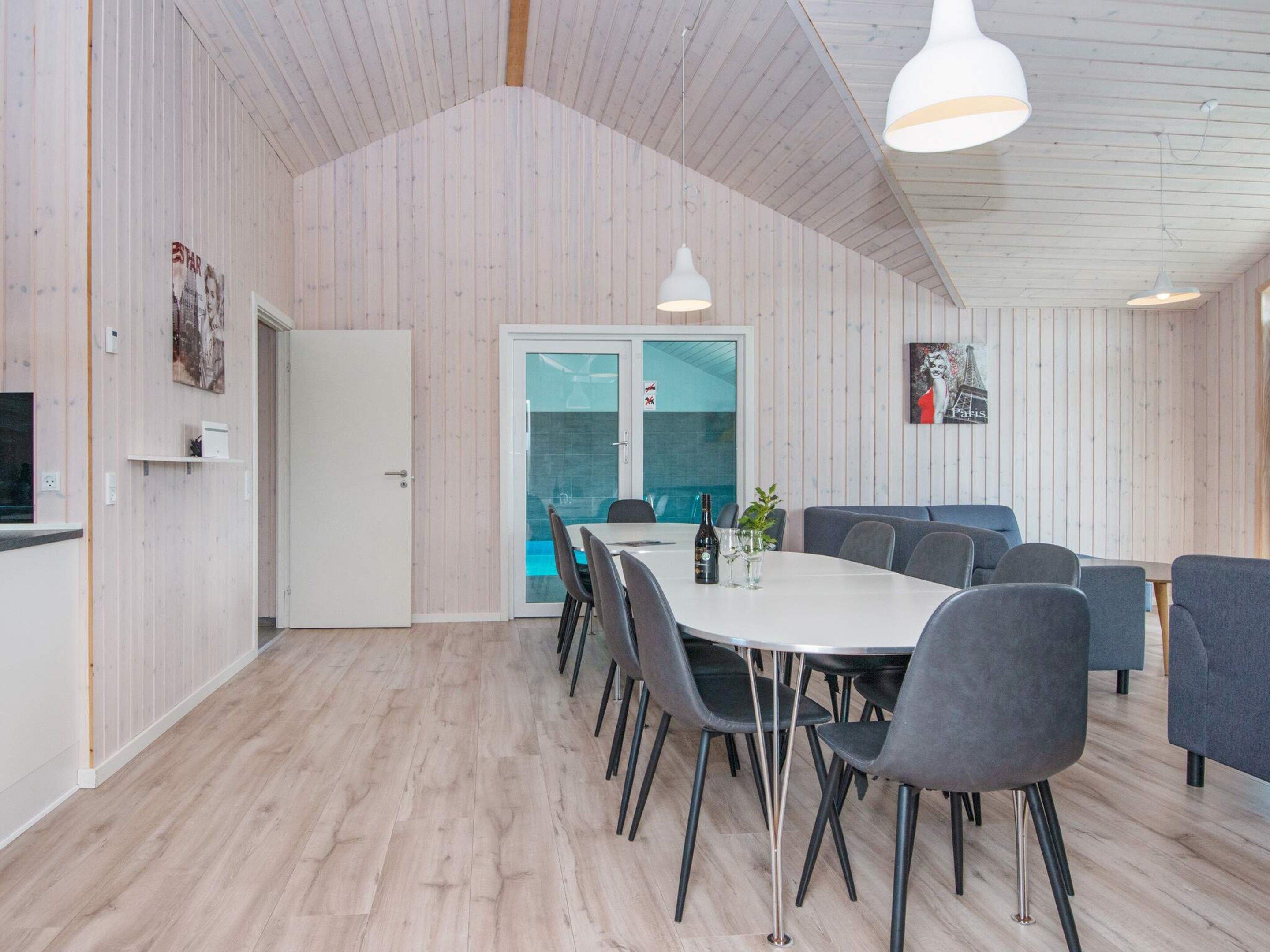 A modern dining area with a white table, grey chairs, and pendant lighting.
