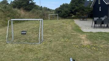 A grassy outdoor area with two soccer goals, a metal fence, and a building with a dark exterior.