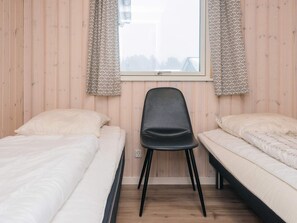 A bedroom with two single beds, a black chair, and a window with patterned curtains. - Holiday Home in RÃ¸mÃ¸ (Rømø)