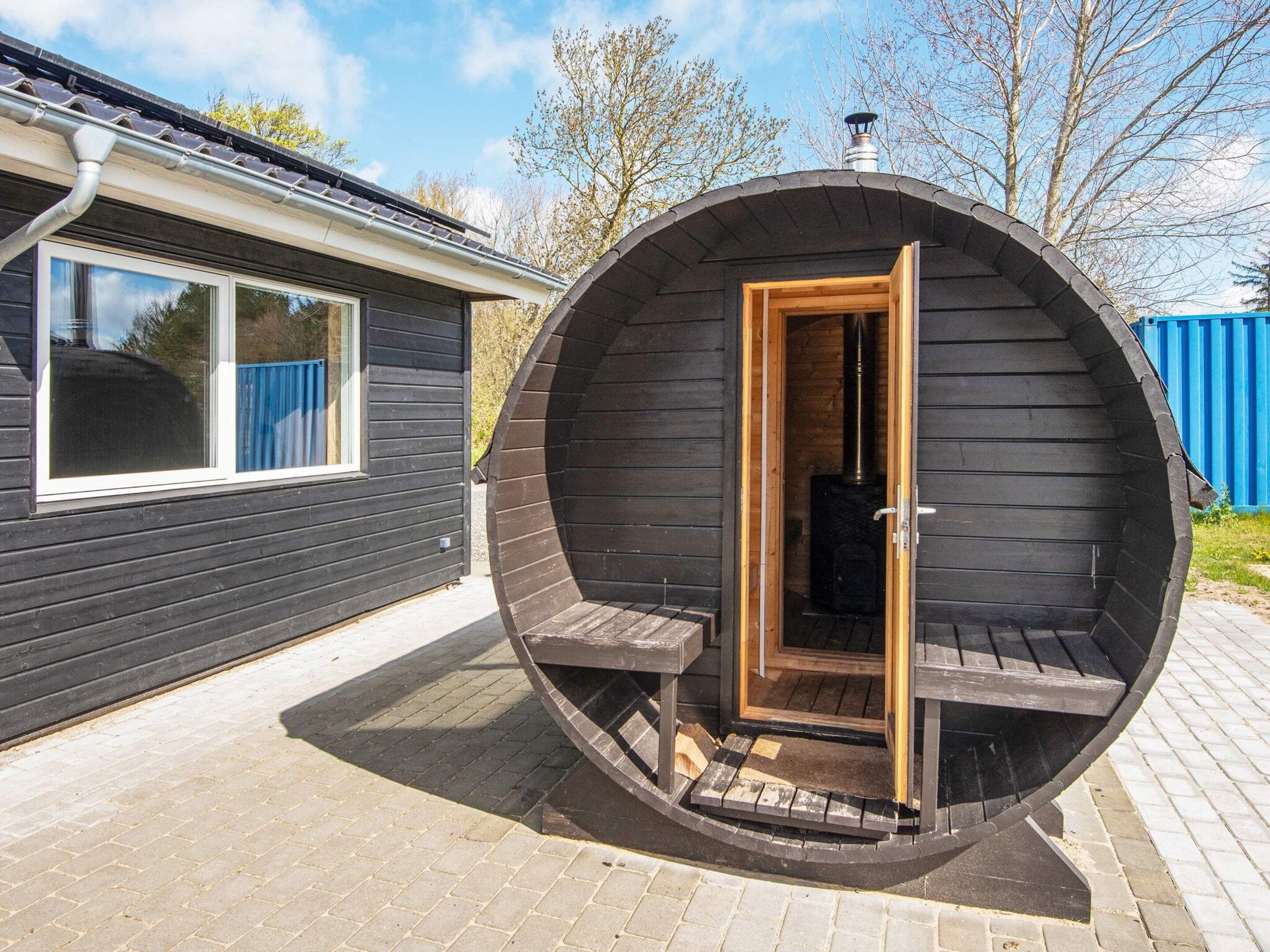 A circular wooden sauna with an open door, a window, and a chimney.