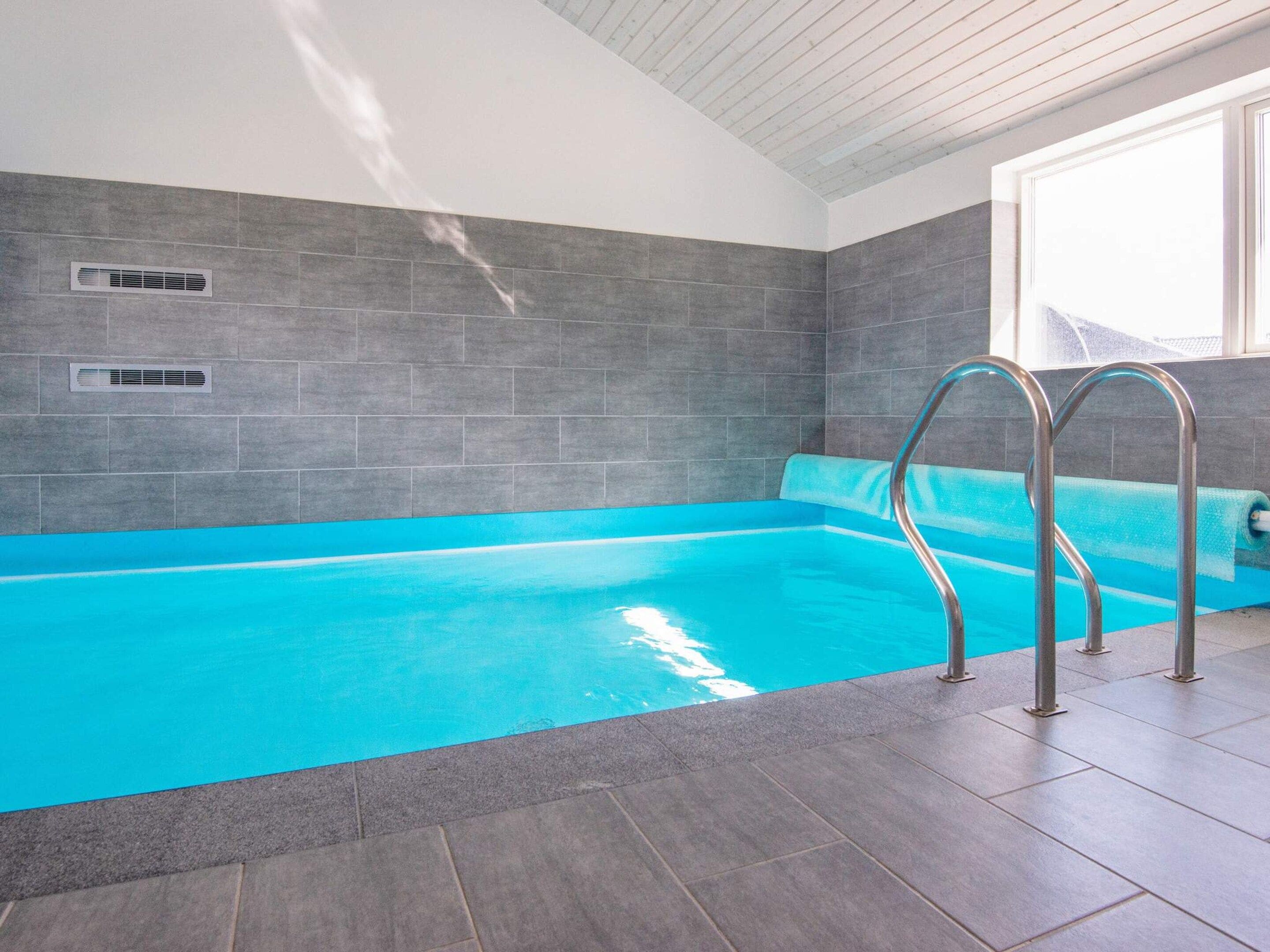 A swimming pool with a blue interior, surrounded by grey tiles, and metal pool ladders.