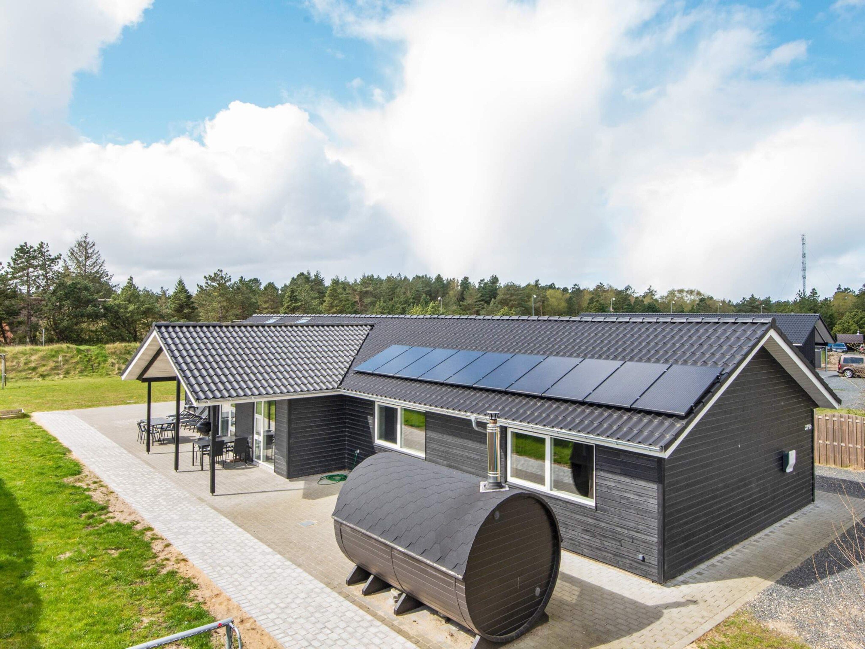 A modern house with a large solar panel array, a covered outdoor seating area, and a cylindrical water tank.