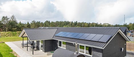 A modern house with a large solar panel array, a covered outdoor seating area, and a cylindrical water tank.