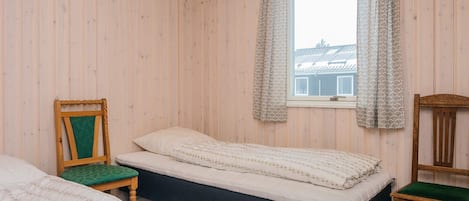 A room with two beds, a window with patterned curtains, and a chair with a green cushion.