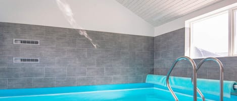 A swimming pool with a clear blue water, surrounded by grey tiles, and metal pool ladders.