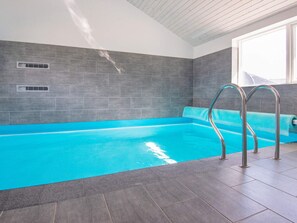 A swimming pool with a clear blue water, surrounded by grey tiles, and metal pool ladders. - Holiday Home in RÃ¸mÃ¸ (Rømø)