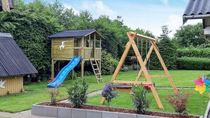 A wooden playhouse with a blue slide and a swing set in a garden.