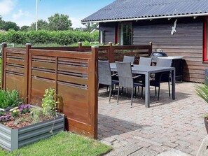 An outdoor patio with a wooden fence, a table with chairs, and a barbecue grill.