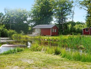 A red cabin with a dock, surrounded by water and greenery.