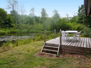 A wooden deck with a table and chairs overlooking a pond surrounded by lush greenery.