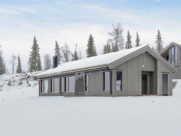 A two-story cabin with a snow-covered roof, large windows, and a stone foundation. - 4 Star Holiday Home in Favang (Ringebu)