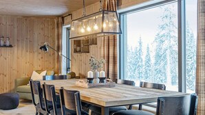 Un intérieur en bois avec une grande table à manger, des chaises, un canapé et une fenêtre donnant sur un paysage enneigé.