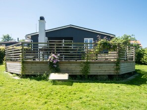 A single-story building with a dark roof, a chimney, and a fenced deck area with plants.