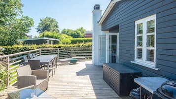 Una terraza con mobiliario exterior, una parrilla y una casa con chimenea.