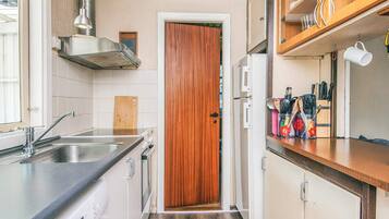 Una cocina compacta con puerta de madera, pileta de acero inoxidable y mesón con utensilios de cocina.