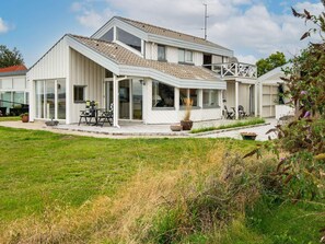 A modern two-story house with a covered patio, large windows, and a well-maintained lawn.