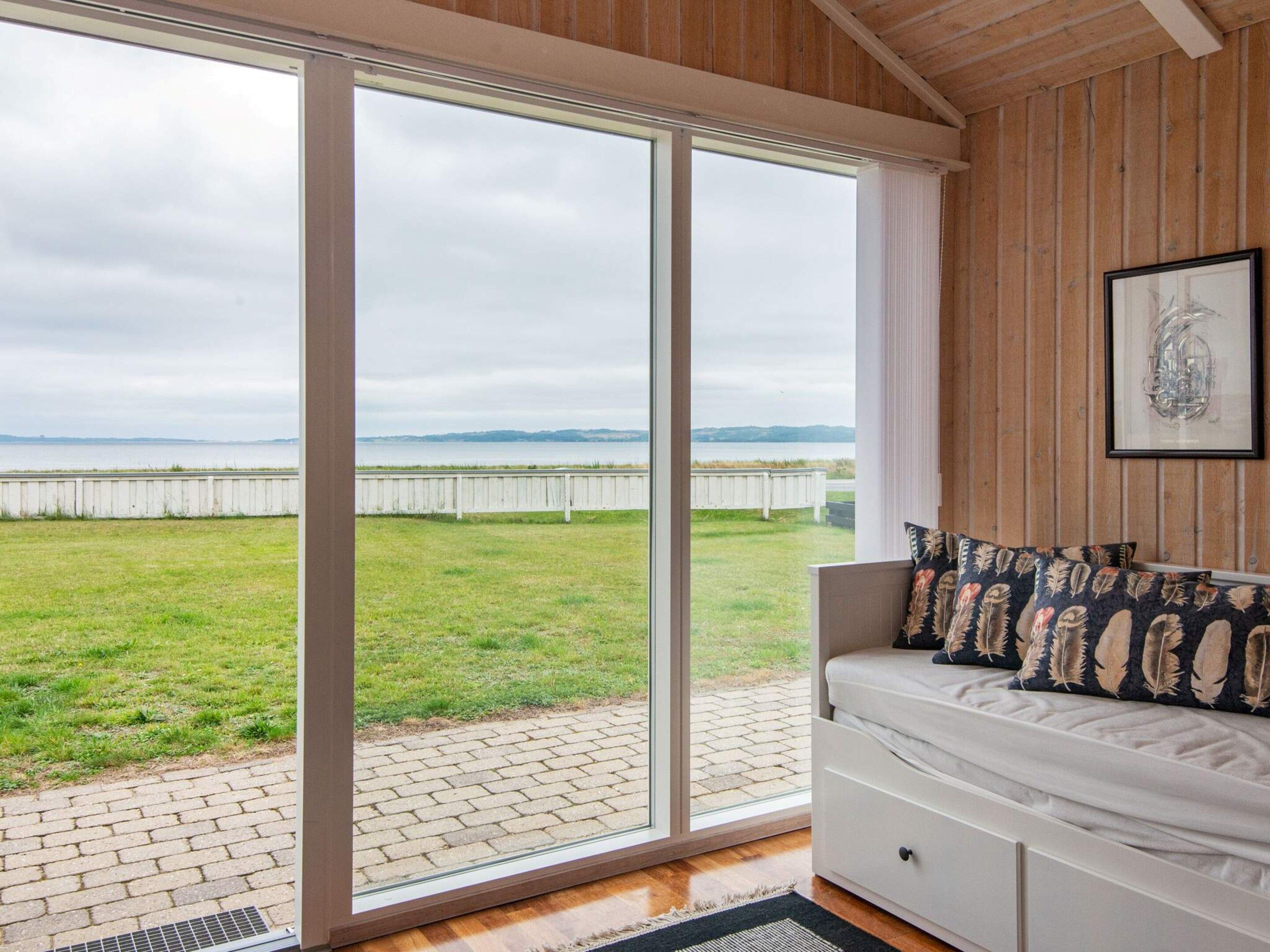 A room with a large sliding glass door leading to a grassy outdoor area, a white sofa with patterned cushions, and a framed picture on the wall.