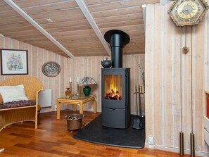 A cozy room with a wood-burning stove, a wicker chair, a small table with a lamp, and a decorative plate on the wall. - 4 Star Holiday Home in Ebeltoft (Ebeltoft)